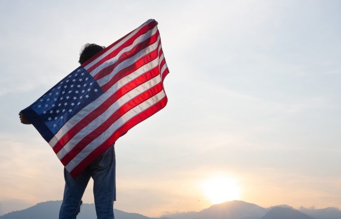 man standing and holding USA flag ิat sunrise view