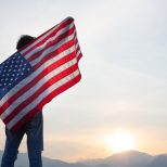 man standing and holding USA flag ิat sunrise view