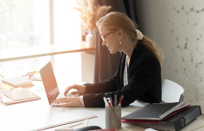 Beautiful ethnic woman in formal suit smiling while having phone conversation and sitting at table in office