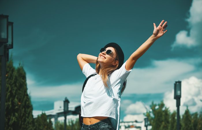 Freedom young woman carefree and happy with open arms on blue sky with hypnotizing sky in background. Caucasian girl in white shirt and jeans, feeling happiness enjoying her travel vacation